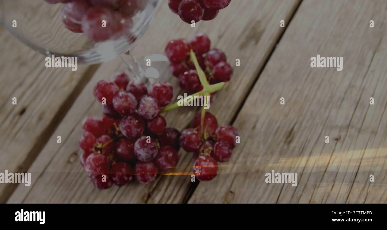 Mostra uve rosse smerigliate appoggiate su un piano in legno rustico, sotto un bicchiere di vino trasparente rovesciato Foto Stock