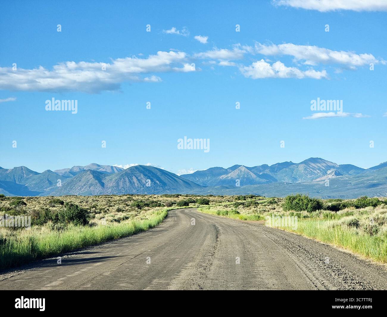 Strada sterrata vuota, strada sterrata attraverso praterie, praterie, deserto verso montagne marroni sotto cielo azzurro con poche nuvole; la strada davanti - Immagine stock catturata con smartphone