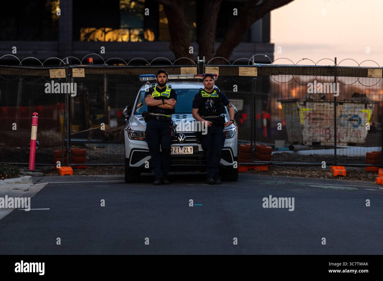 Gli agenti di sicurezza riposano sul cofano di un'auto della polizia posizionata in una strada chiusa fuori dalla sede della conferenza ALP. I manifestanti si riuniscono al di fuori della Conferenza del Partito Laburista Australiano (ALP) all'ippodromo di Moonee Valley, esprimendo opposizione alle politiche governative federali e statali. La manifestazione richiede il riconoscimento immediato della Palestina, la fine dei legami militari con Israele, la protezione dell'edilizia popolare e la difesa dei diritti dell'unione. Organizzata da gruppi di base tra cui la Free Palestine Coalition Naarm e i sostenitori dell'edilizia popolare, la protesta condanna anche le leggi anti-protesta e la dea indigena Foto Stock