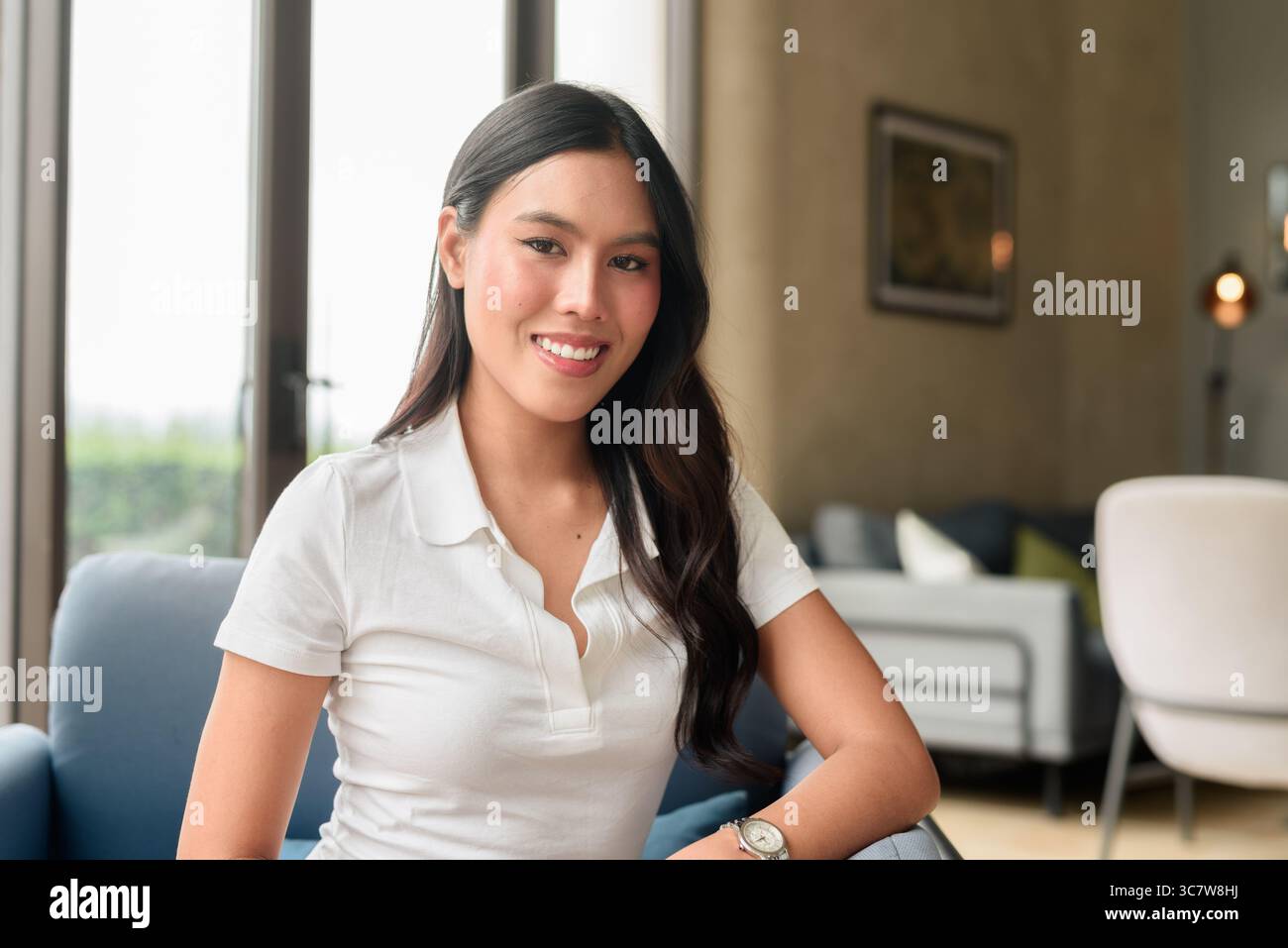 Bella giovane donna asiatica che indossa una polo bianca in posa all'interno dell'hotel o della sala ristorante. Ritratto di stile di viaggio rilassato con interni moderni Foto Stock
