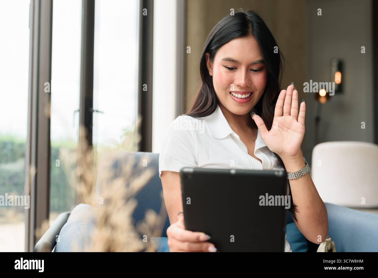 Un giovane e bellissimo turista asiatico che usa un tablet mentre si siede nell'hotel o nella caffetteria lounge. Stile di vita digitale informale ed elegante con interni moderni Foto Stock
