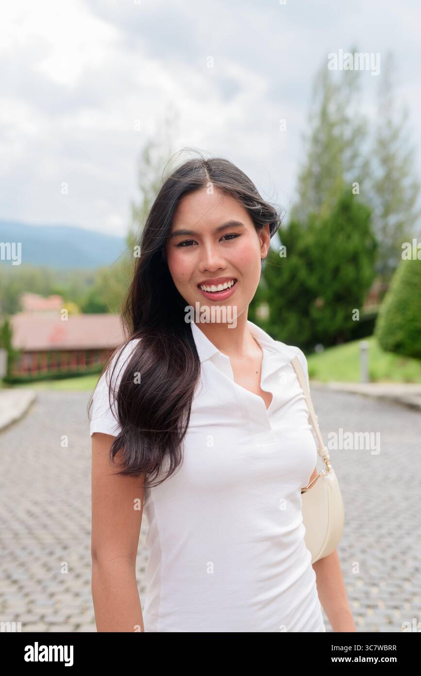 Bella giovane donna asiatica in una polo che cammina lungo la vecchia strada in stile europeo. Elegante ritratto di viaggio circondato da architettura, ad esempio naturale Foto Stock