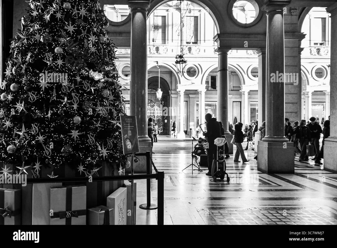 Bianco e nero. Albero di Natale nella galleria dello shopping Galleria San Federico, con un musicista di strada e gente che cammina in via Roma, Torino, Piemonte Foto Stock