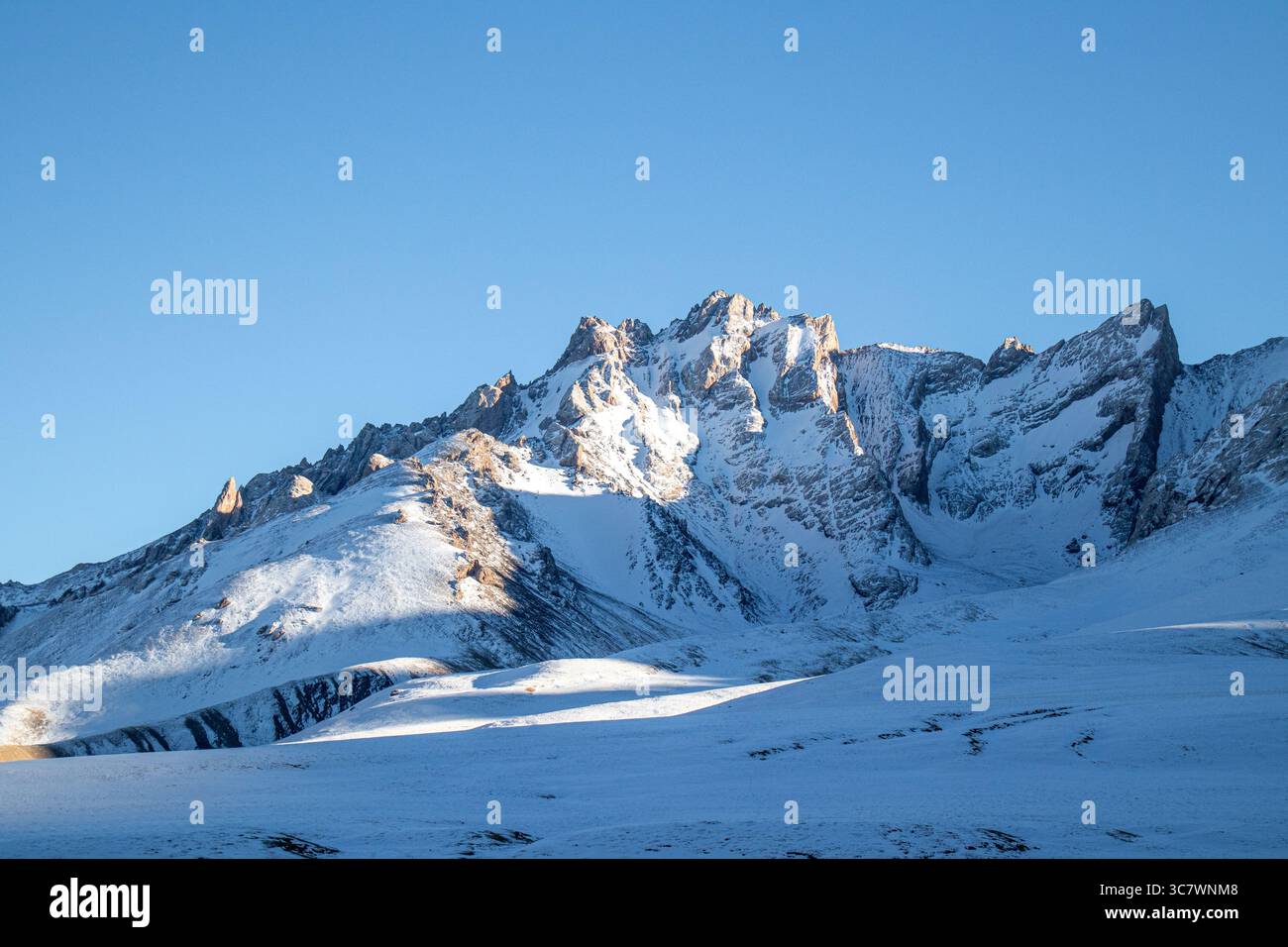 Le maestose cime rocciose innevate si innalzano su un cielo azzurro e limpido, con pendii innevati in primo piano Foto Stock