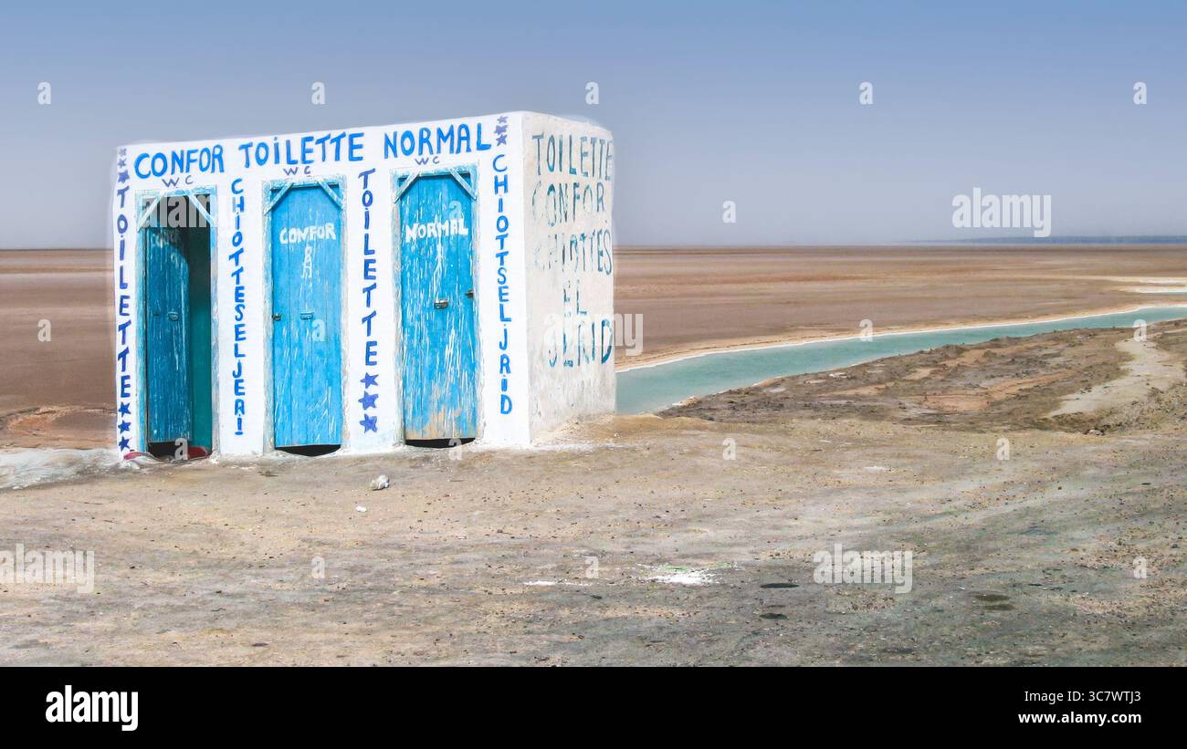 Un vero bagno sulla strada dipinto con segni stravaganti, che si trova da solo nel vasto deserto di sale di Chott el Djerid, Tunisia. Un viaggio funzionale ma surreale st Foto Stock