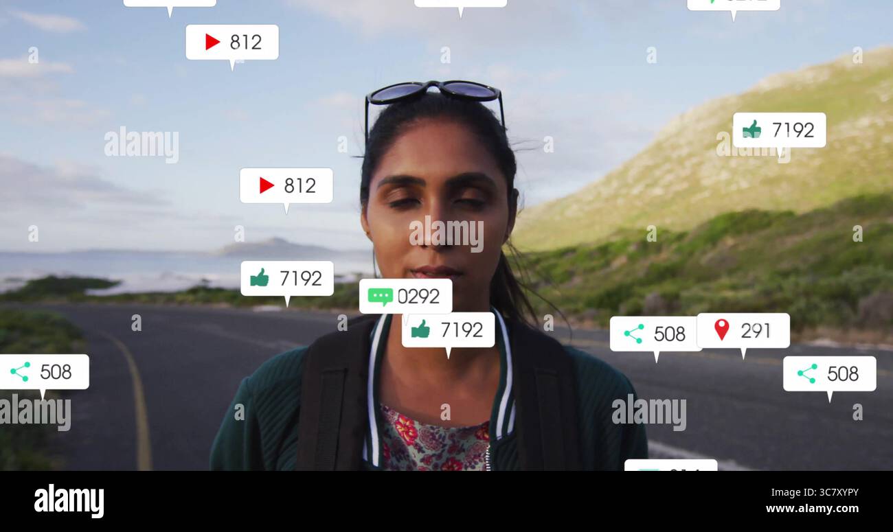 Vlogger da viaggio in piedi che indossa bomber e zaino sull'autostrada costiera, con icone sociali Foto Stock
