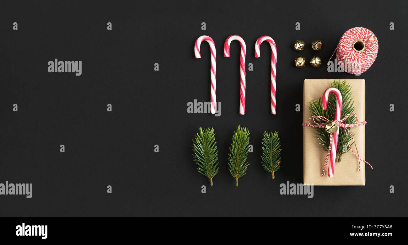 Confezione regalo artigianale con canna da zucchero, abete rosso e campana jingle su sfondo nero. Vista dall'alto, copyspace. Foto Stock