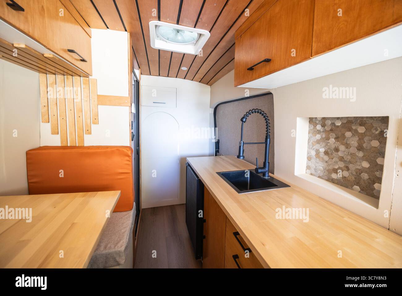 Vista interna di un camper dal design caldo e accogliente, con accenti in legno e luci soffuse per un'atmosfera casalinga. Foto Stock