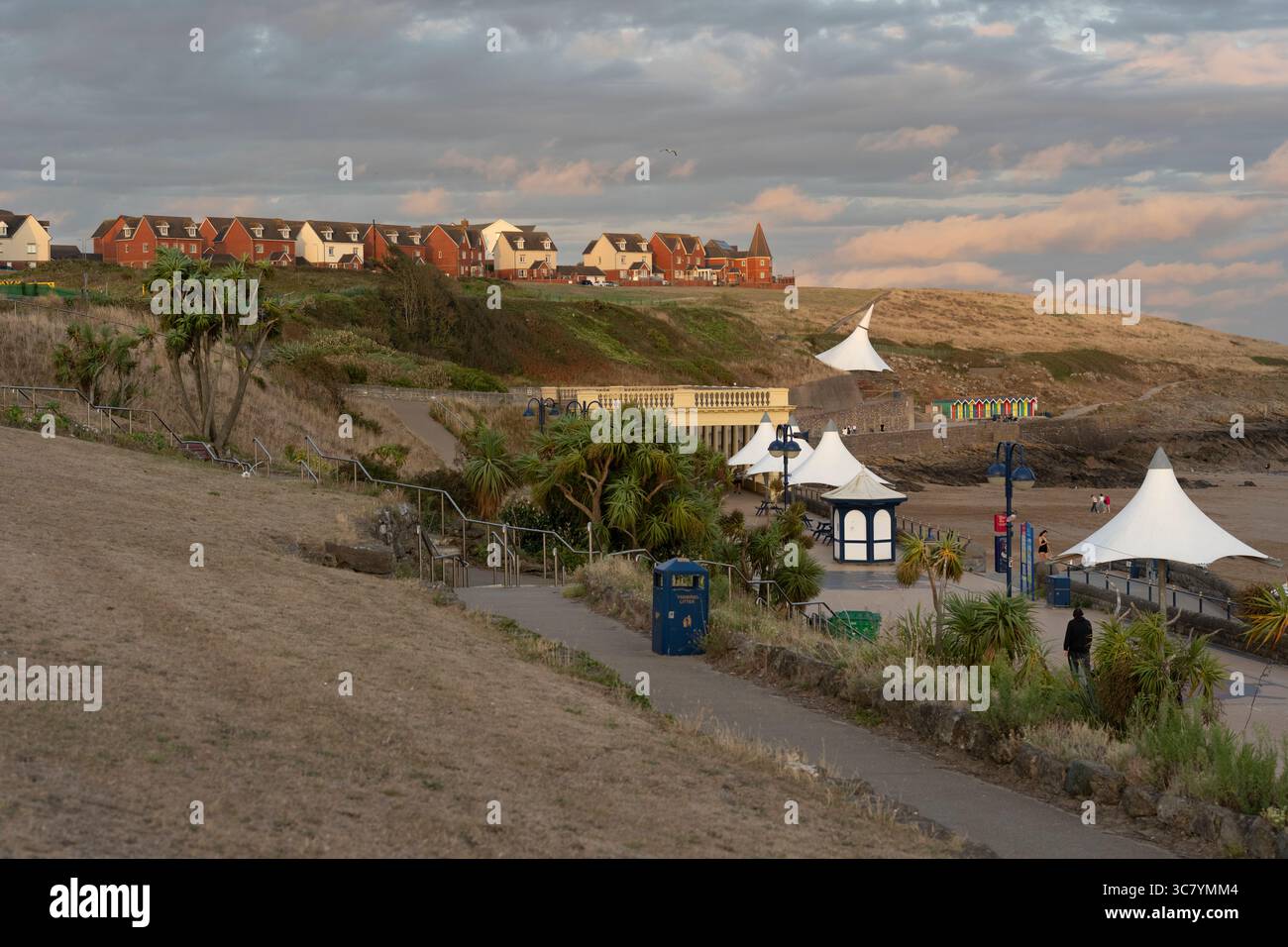 Una vista panoramica di Barry Island, Galles, con la passeggiata con le sue iconiche baldacchini bianche e le colorate capanne sulla spiaggia. La gente passeggia lungo la spiaggia Foto Stock