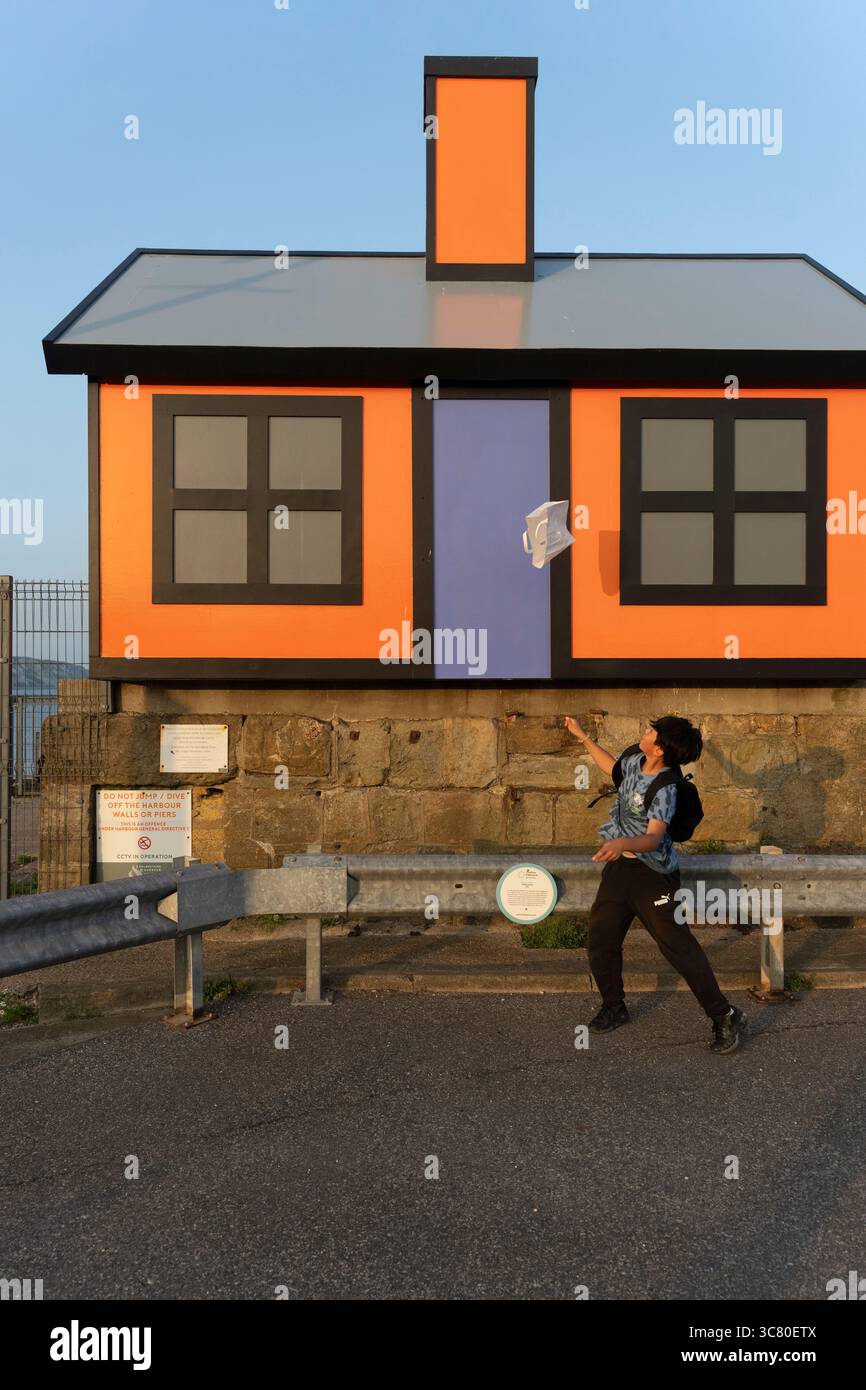 Un ragazzo getta la spazzatura all'installazione artistica "House" di Folkestone Harbour Arm. Sta spargendo e deturpando l'arte pubblica. Foto Stock