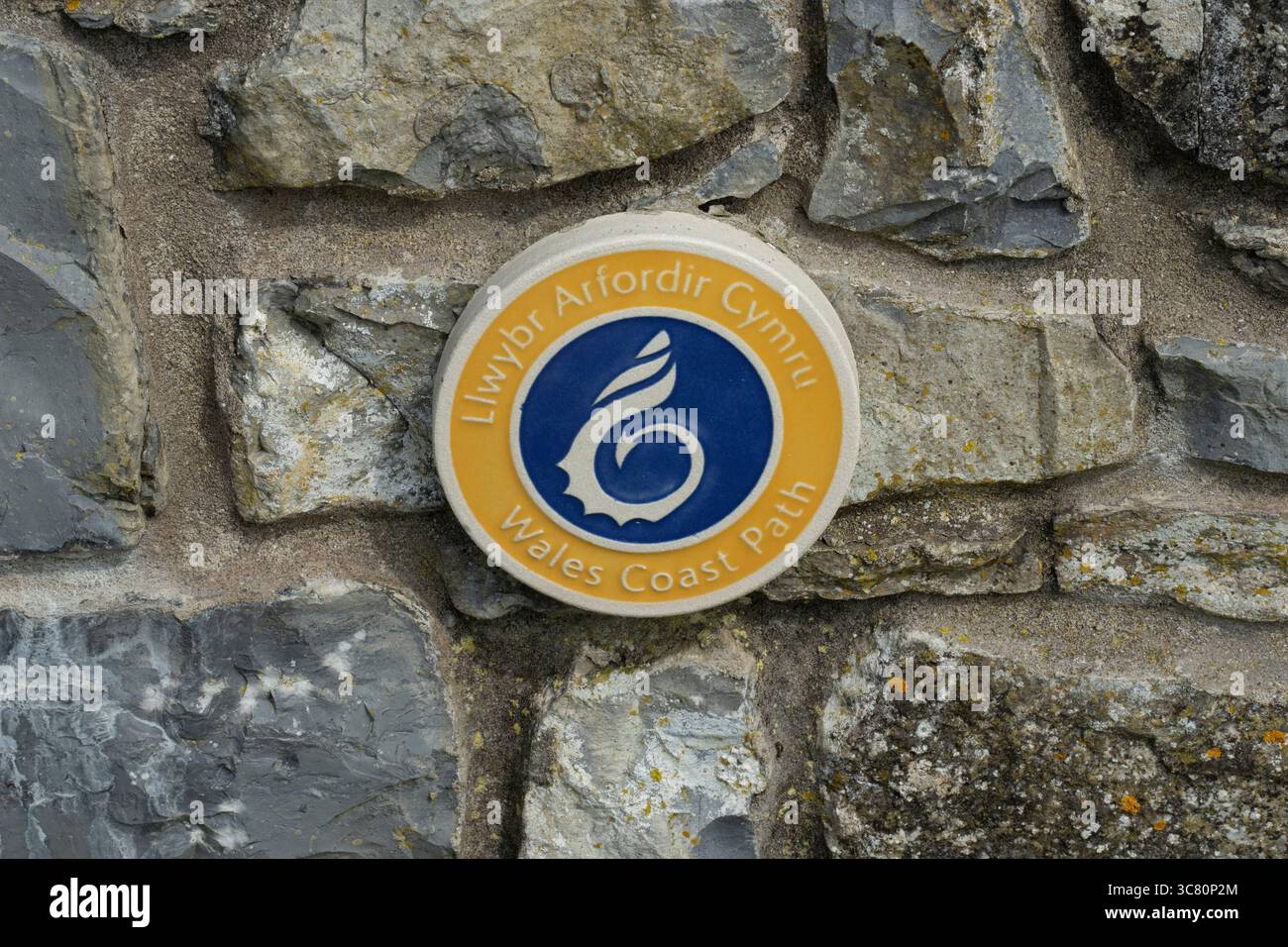 Un cartello del Wales Coast Path è apposto su un muro di pietra. Il cartello aiuta gli escursionisti a navigare lungo la panoramica costa gallese. Foto Stock