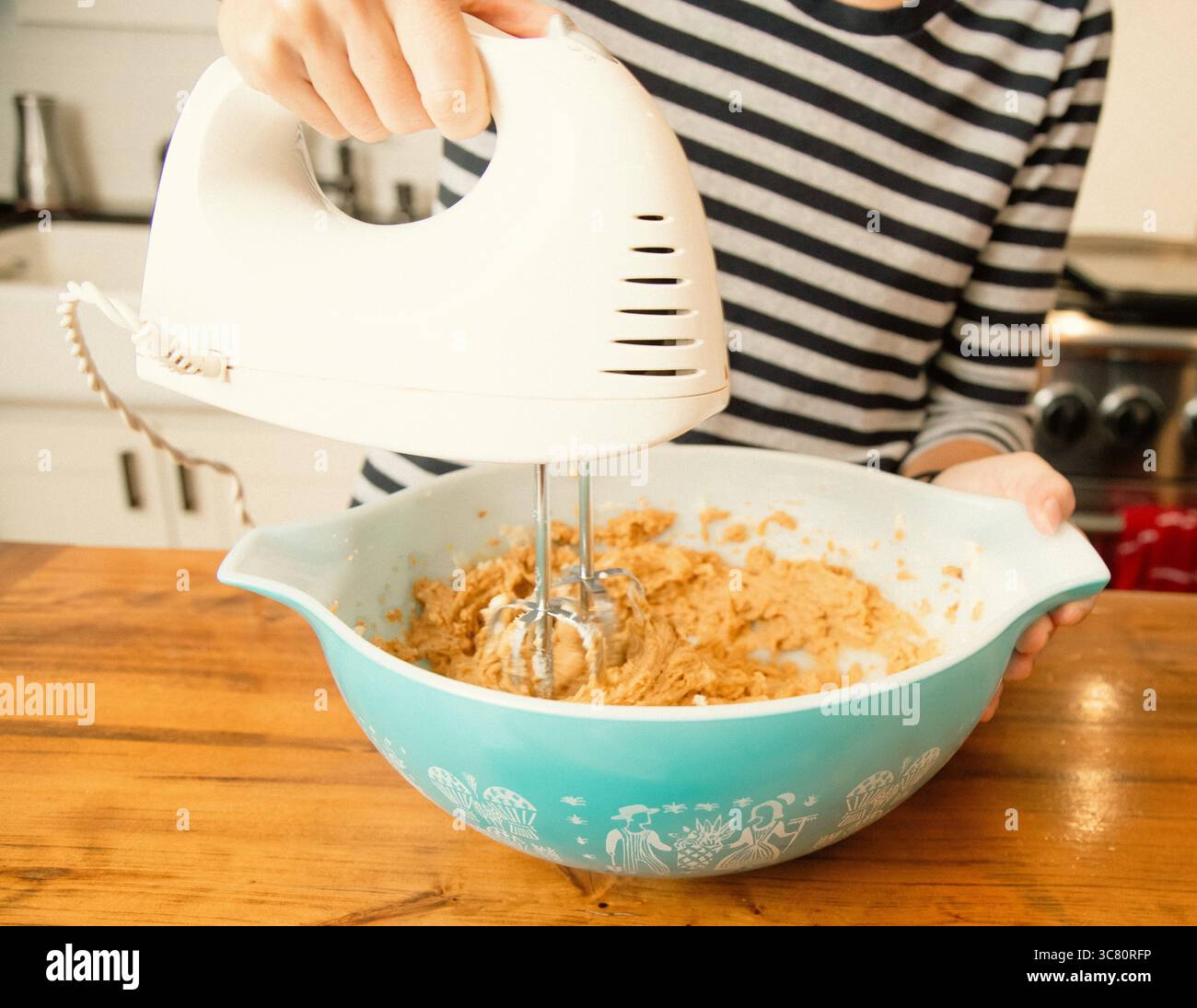 Primo piano di una donna adulta in cucina che mescola l'impasto in un recipiente con una frusta elettrica Foto Stock