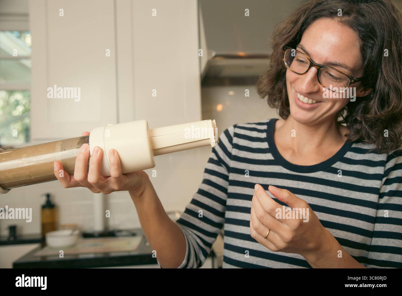 Donna sorridente di mezza età in piedi in una cucina con una pressa per biscotti piena Foto Stock