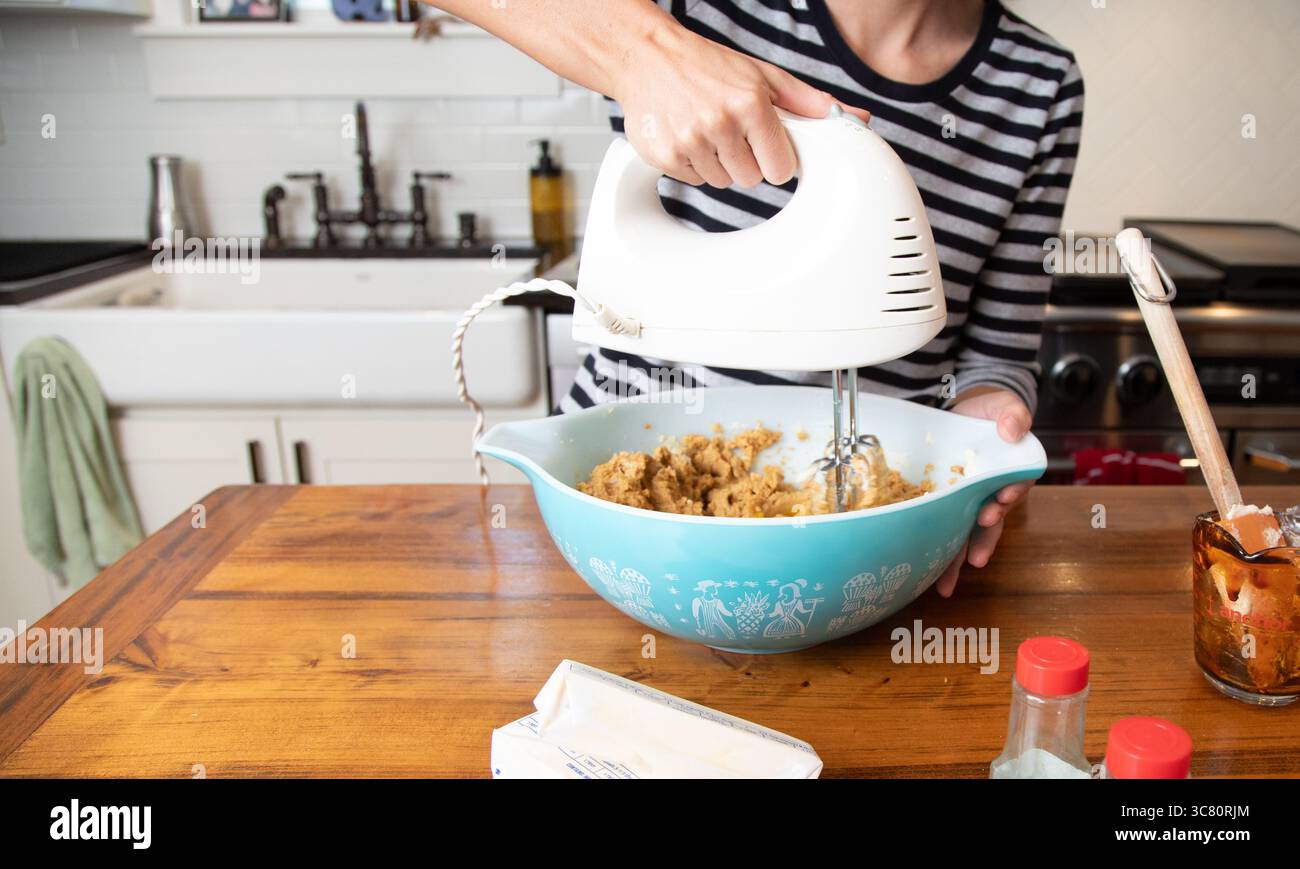 Primo piano di una donna adulta in cucina che mescola l'impasto in un recipiente con una frusta elettrica Foto Stock