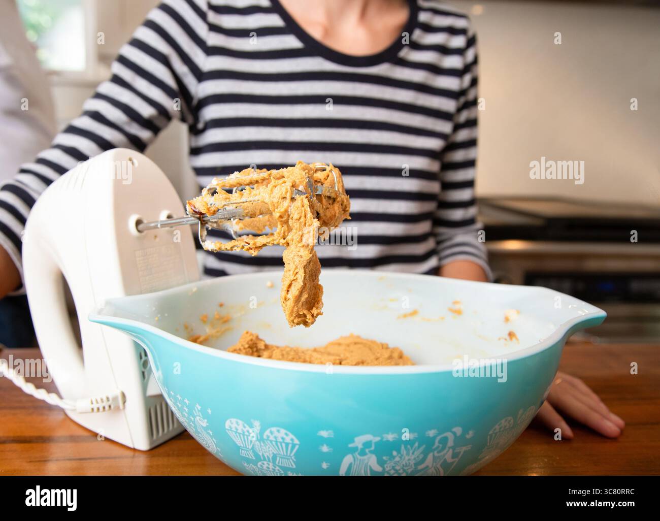 Primo piano di una donna adulta in cucina che mescola l'impasto in un recipiente con una frusta elettrica Foto Stock