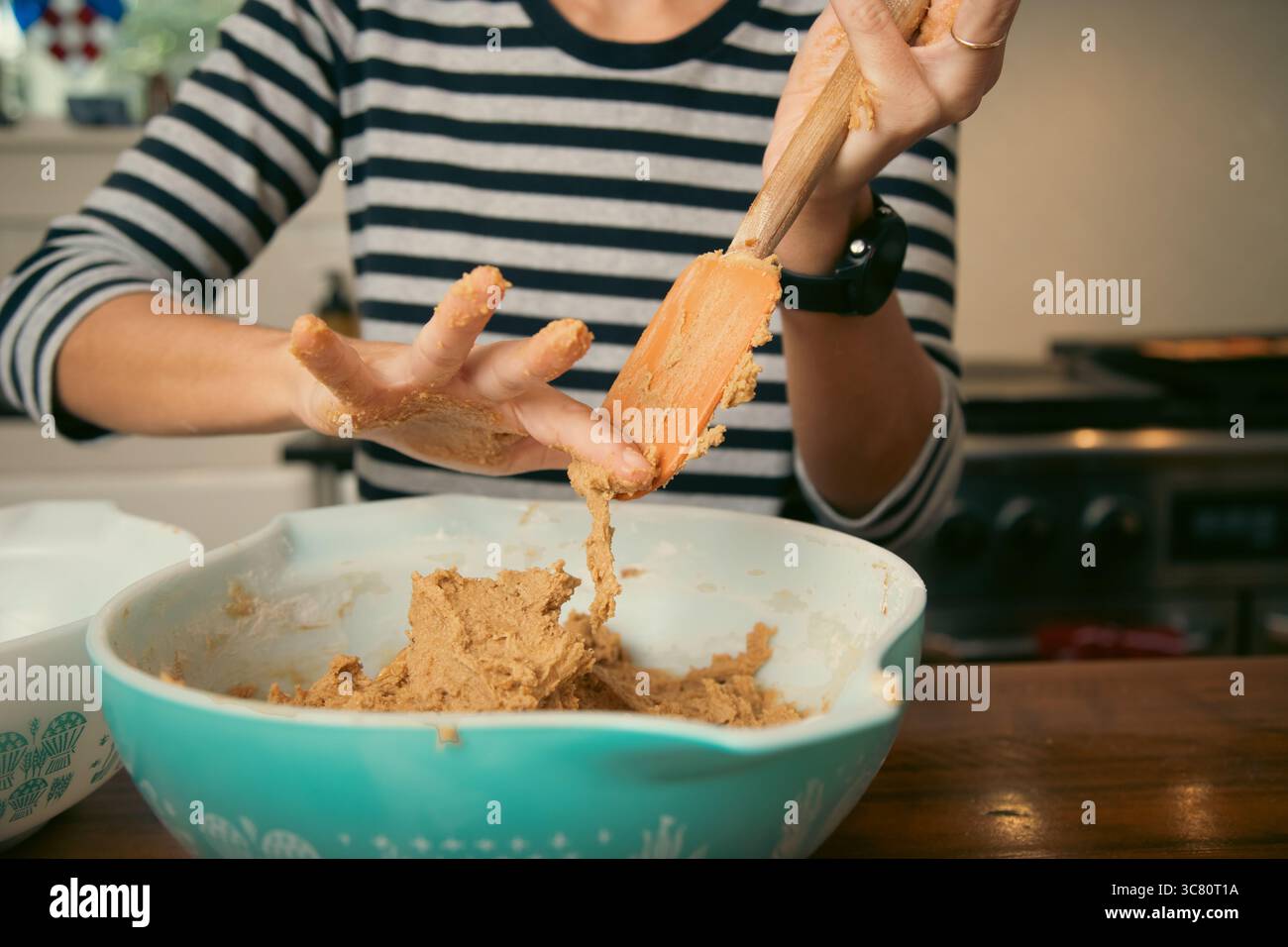 Primo piano di una donna adulta in una cucina che raschia con il dito l'impasto crudo da una spatola Foto Stock