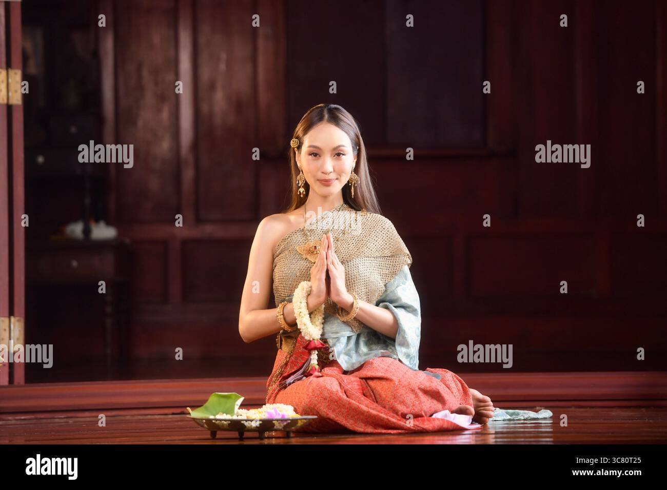Ritratto di una giovane donna che indossa abiti tradizionali thailandesi seduti sul pavimento con offerte religiose in preghiera Foto Stock