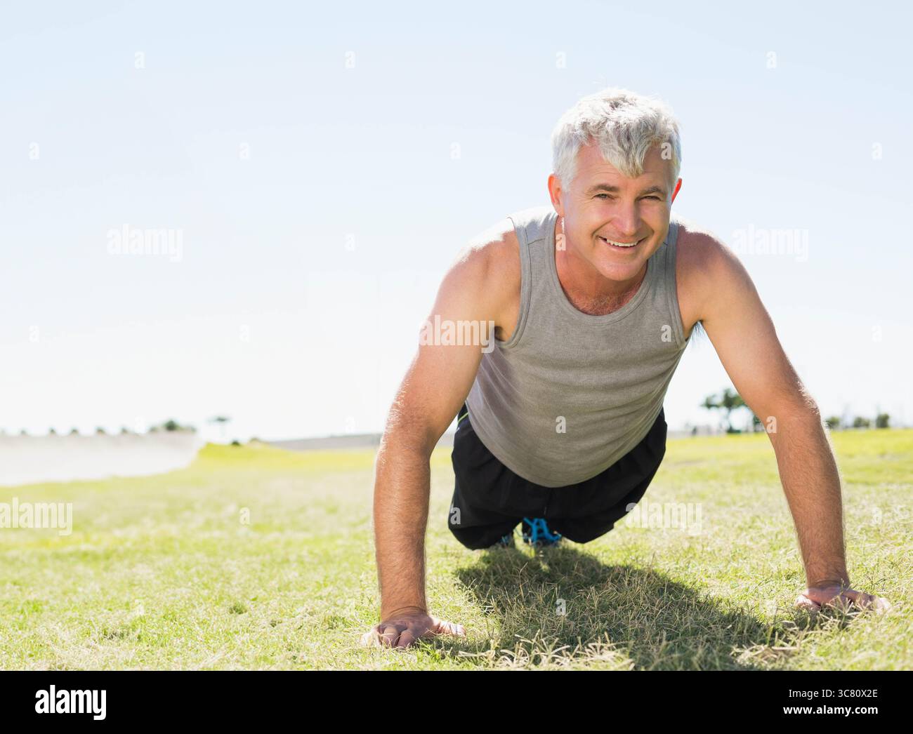 Push-up da uomo senior sul campo in erba con canotta grigia e sneaker con dettagli blu Foto Stock