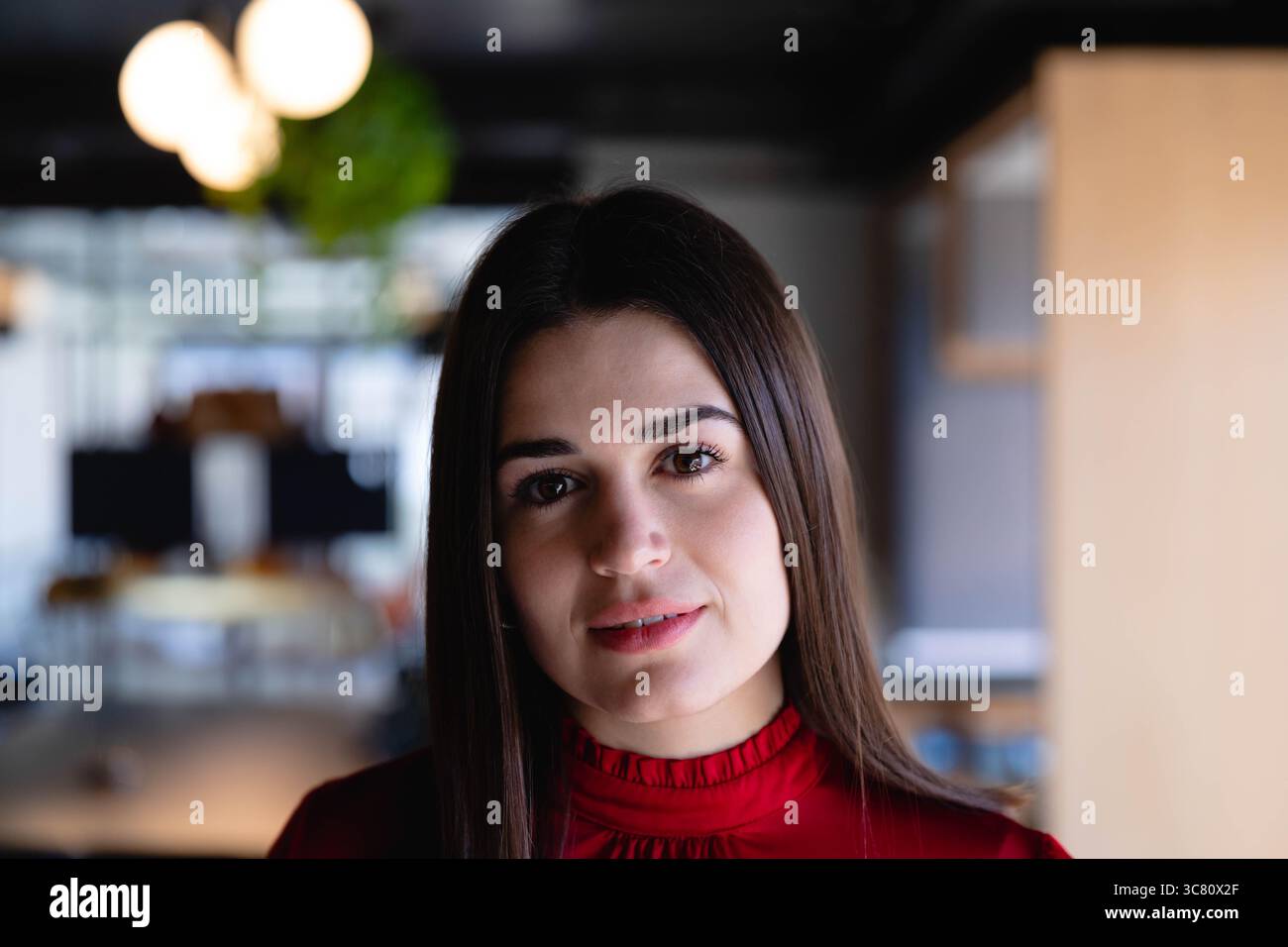 Donna che lavora in un ufficio open space con indosso una camicetta rossa tra scrivanie monitor di computer e impianti Foto Stock