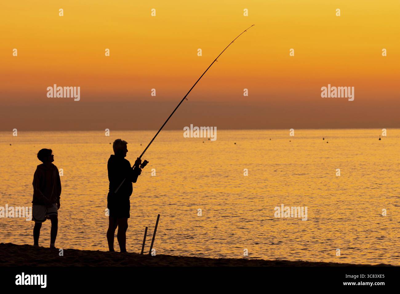 Un uomo che pesca proprio di fronte all'alba sulla Costa Rei, una costa dell'isola italiana della Sardegna, nel Mar Mediterraneo, Monte Nai, Costa Rei Foto Stock