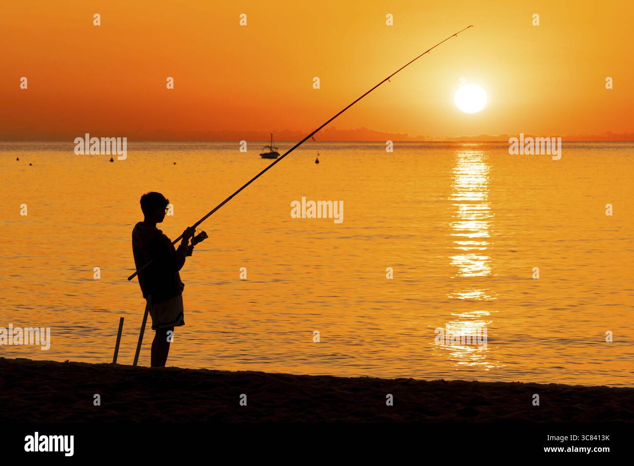 Un ragazzo che pesca poco dopo l'alba sulla Costa Rei, una costa dell'isola italiana della Sardegna, nel Mar Mediterraneo, Monte Nai, Costa Rei, S. Foto Stock