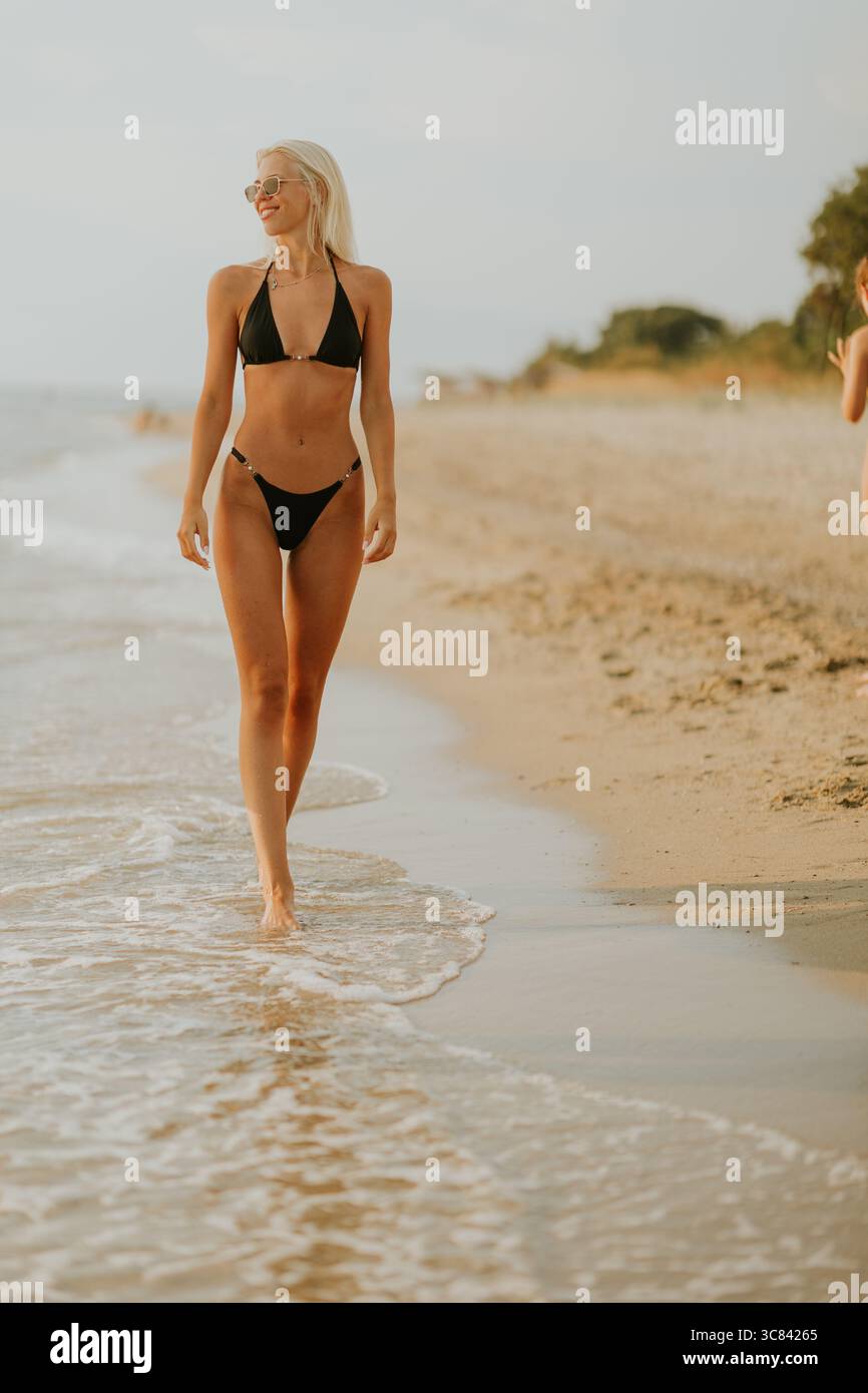 Un gruppo di amici fa una piacevole passeggiata lungo la costa durante il tramonto. La spiaggia è dorata, con dolci onde che si infrangono ai piedi, creando Foto Stock