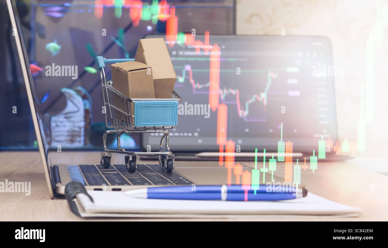 Mini carrello con pacchi sulla tastiera del notebook, grafici delle azioni sovrapposti, simbolo dello shopping online e delle tendenze del trading finanziario. Foto Stock
