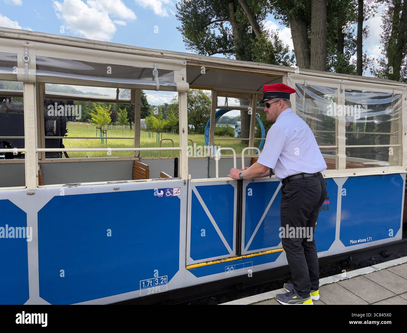 Operaio ferroviario presso la stazione ferroviaria di Maltanka a scartamento ridotto di Poznań, Polonia. Apertura di porte di trasporto per i passeggeri in un giorno d'estate. Foto Stock