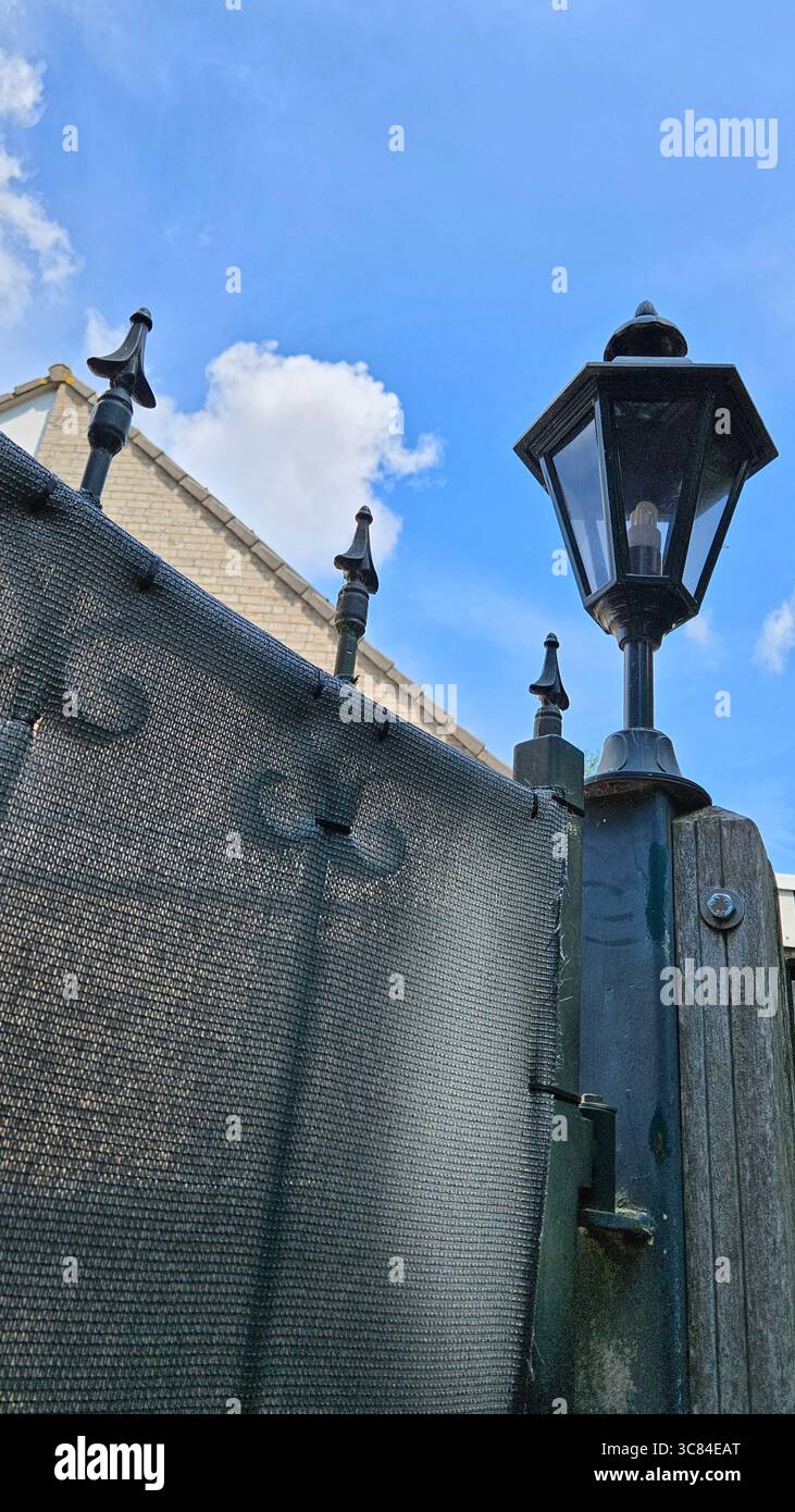 Primo piano di una recinzione in ferro battuto e palo lampada in stile lanterna d'epoca, sullo sfondo di un edificio tradizionale con tegole in terracotta. Foto Stock