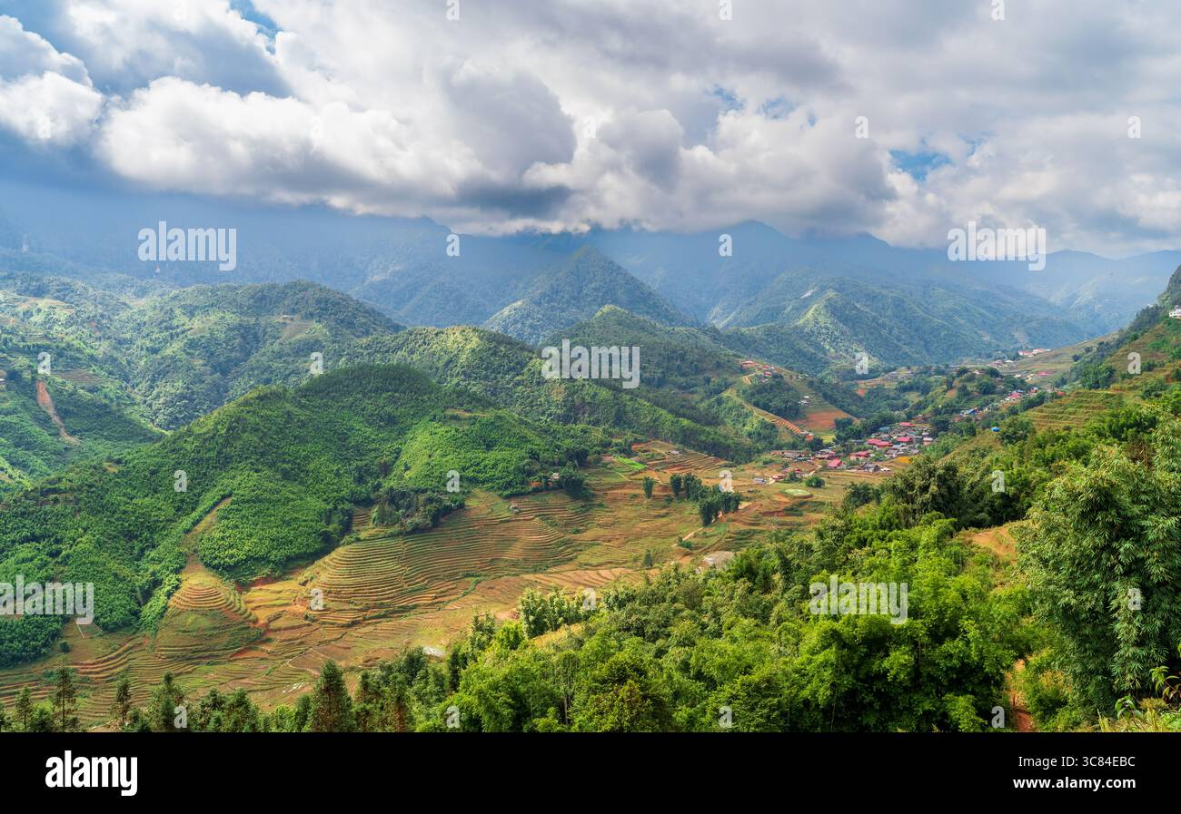 Paesaggio panoramico di risaie terrazzate e catene montuose a Sapa, Vietnam, con tradizionali case di villaggio annidate tra le colline sotto il suggestivo paesaggio Foto Stock