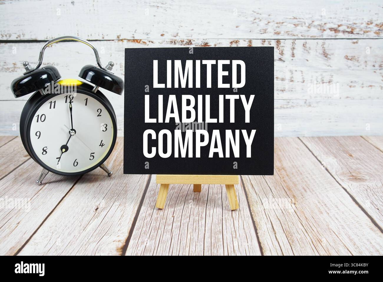 Testo della società a responsabilità limitata con cavalletto e sveglia su sfondo in legno Foto Stock
