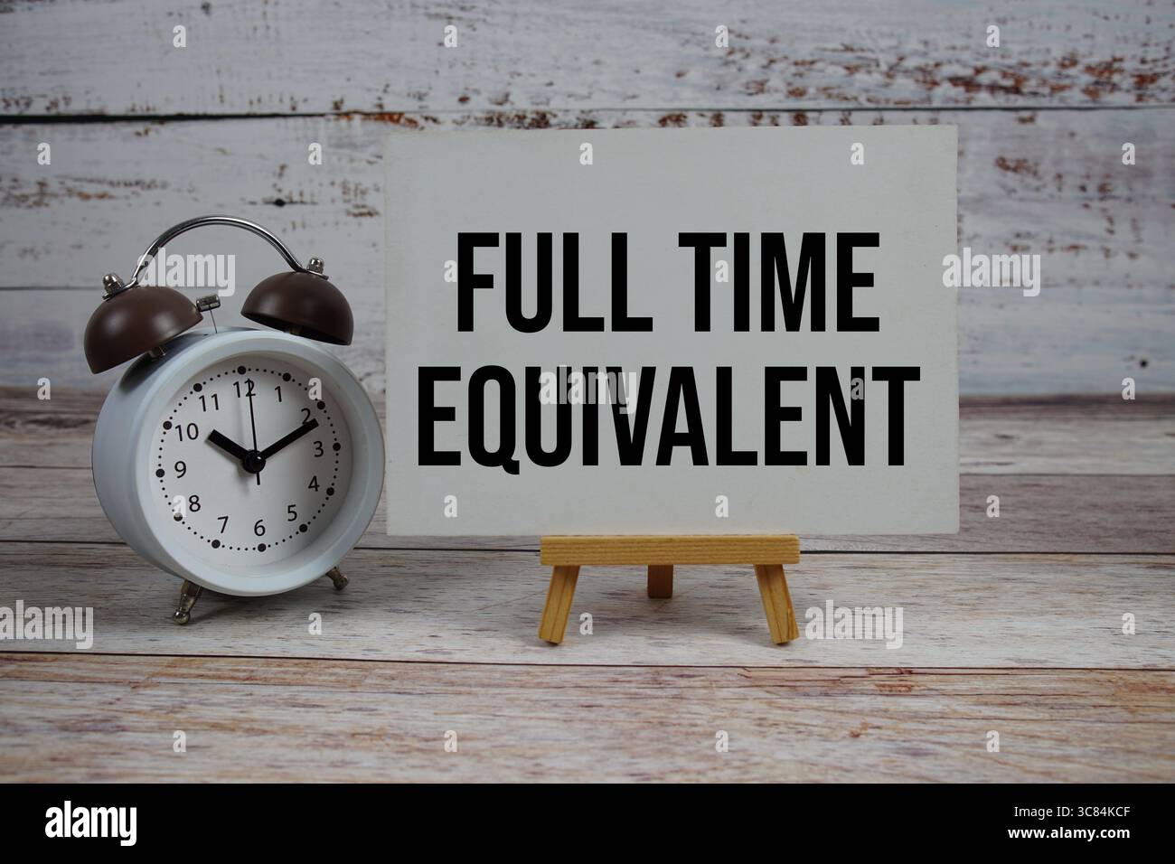 Testo equivalente a tempo pieno con cavalletto e sveglia su sfondo in legno Foto Stock