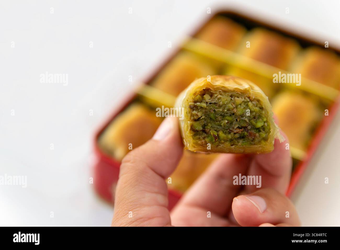 Primo piano di Pistacchio Baklava tenuto in mano, scatola di dolci su sfondo bianco Foto Stock