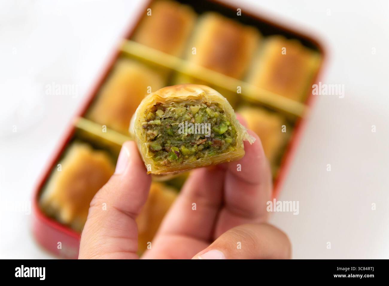 Primo piano di Pistacchio Baklava tenuto in mano, scatola di dolci su sfondo bianco, piatto, spazio copia Foto Stock