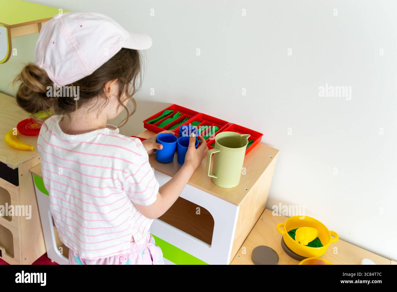 bambini che sistemano tazze e una caraffa su un bancone in legno della cucina, con piatti e utensili. concetto di gioco fantasioso, educati della prima infanzia Foto Stock