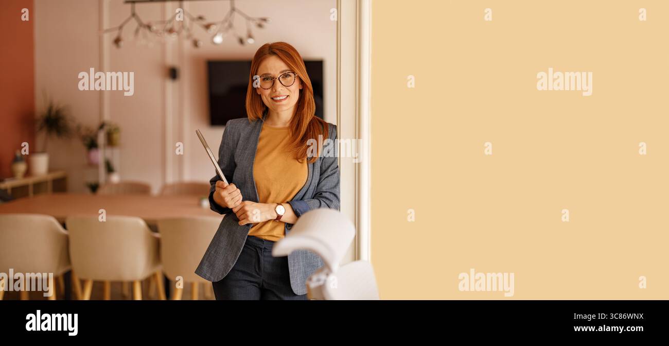 Ritratto di avvocato donna in occhiali da vista con computer e in piedi con sicurezza a parete in un ufficio moderno Foto Stock