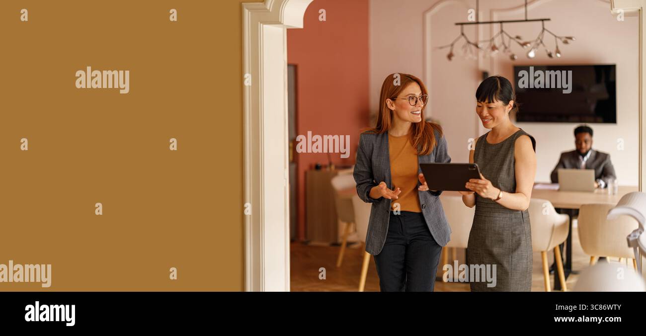 Donne imprenditrici che camminano e discutono idee mentre esaminano i dati aziendali su un tablet digitale in ufficio Foto Stock