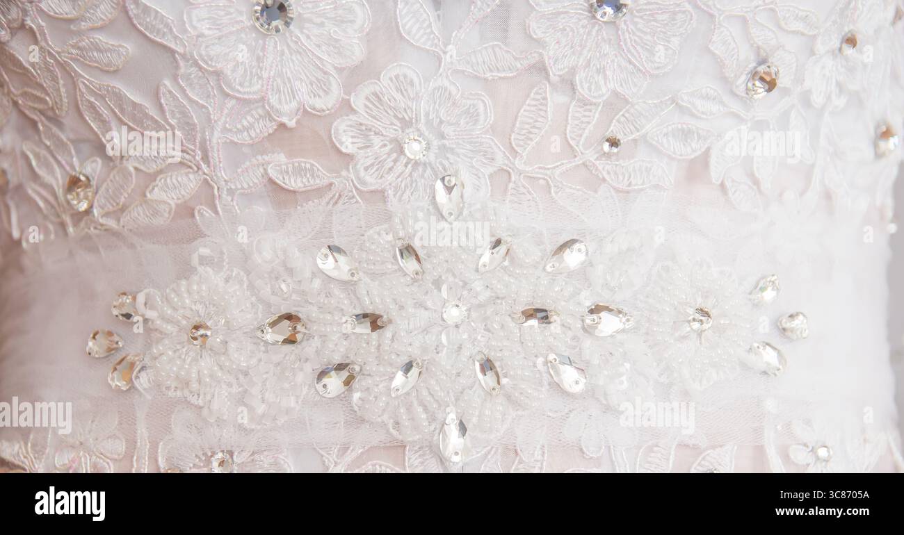 Elegante dettaglio in pizzo bianco con ricami floreali e sfavillanti decorazioni su un abito da sposa Foto Stock