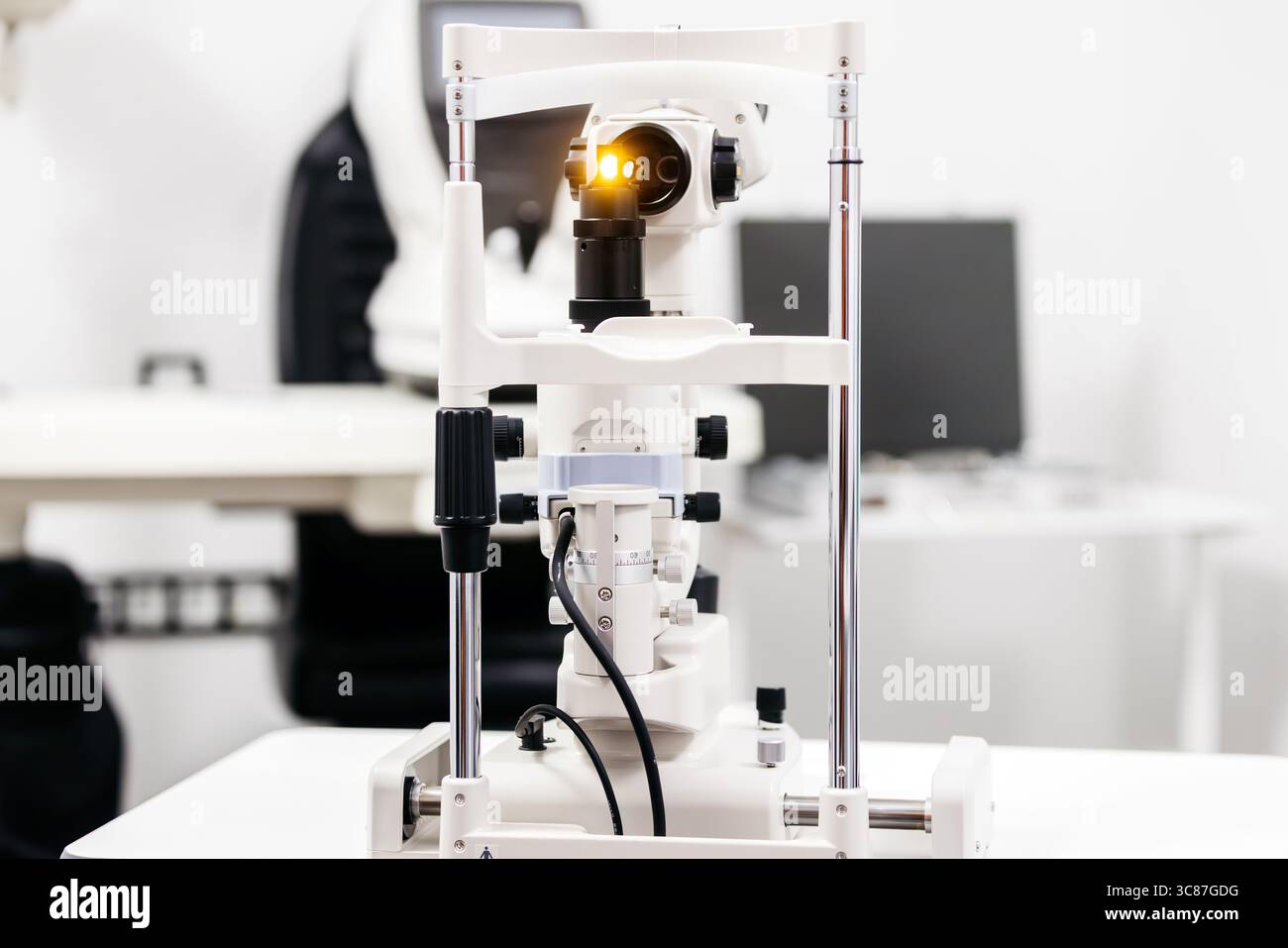 L'apparecchiatura per esami oftalmici include una lampada a fessura con lente illuminata, posizionata su un tavolo clinico in una moderna struttura oculistica, evidenziando l'annuncio Foto Stock