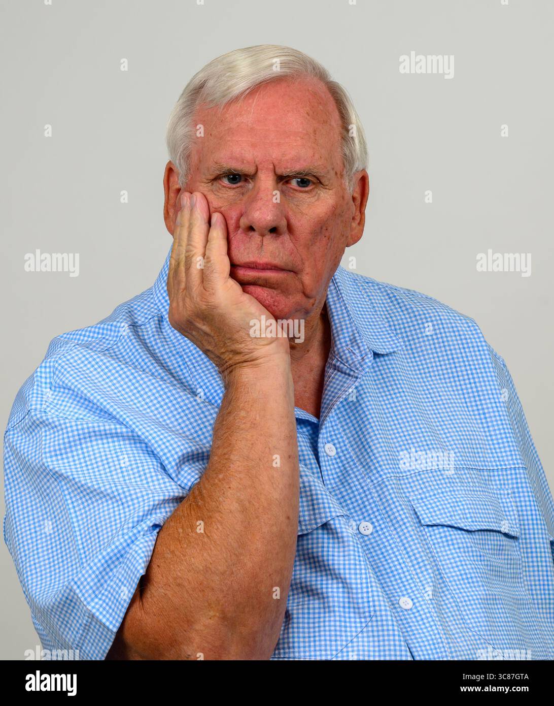 L'uomo più anziano che indossa una camicia a scacchi blu e bianca con la mano sul mento sembra essere in profondo pensiero Foto Stock