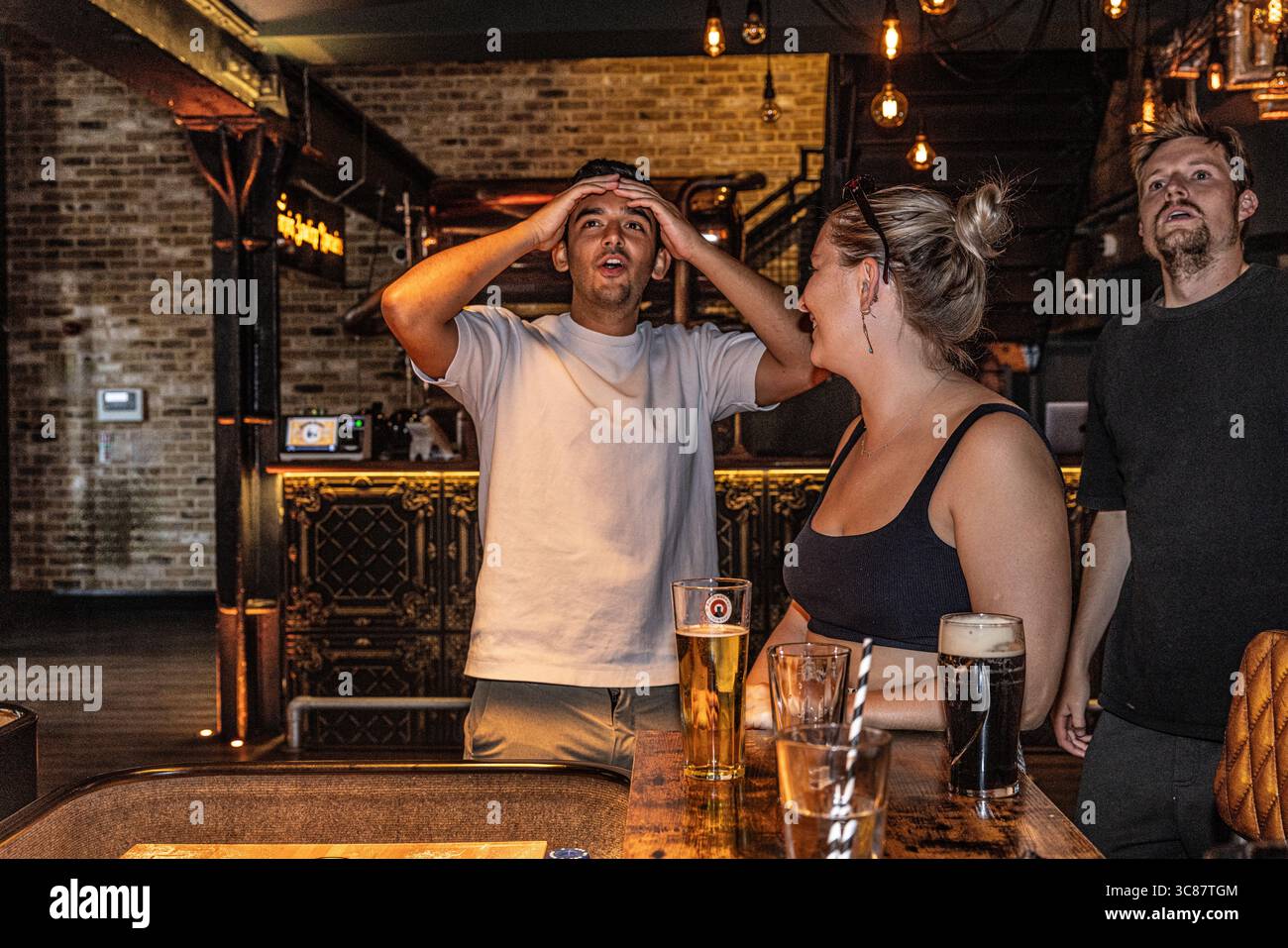 Giovane uomo che reagisce con delusione dopo aver perso una partita di shuffleboard, tenendo le mani sulla testa con incredulità. Foto Stock
