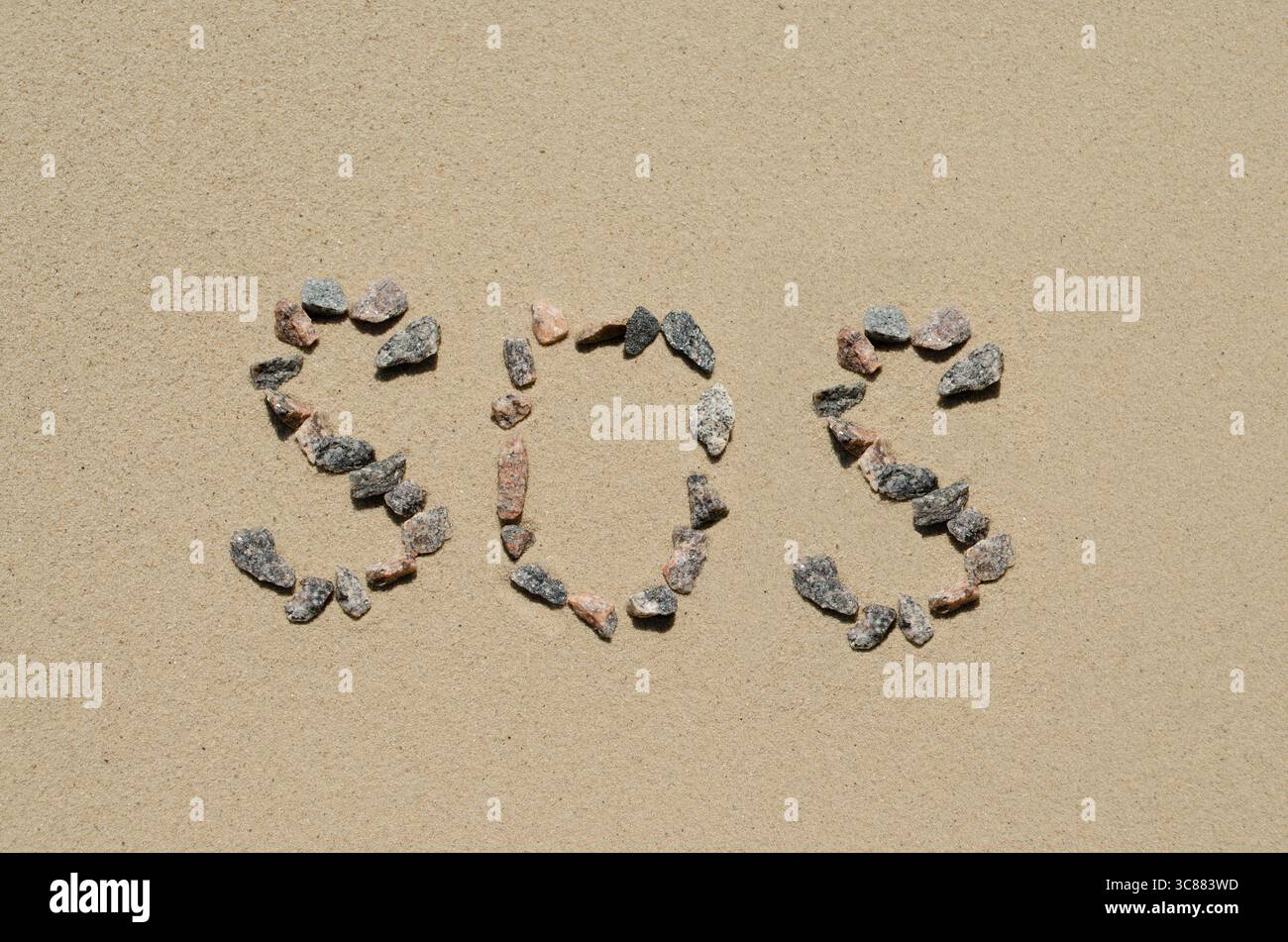 Messaggio SOS scritto con rocce sulla sabbia Foto Stock