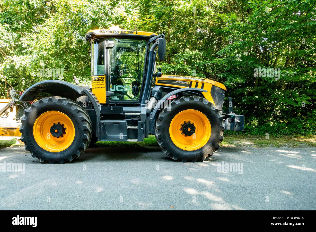 Trattore giallo e nero JCB Fastrac parcheggiato accanto agli alberi forestali in una giornata di sole, ruote grandi e macchinari agricoli moderni. Foto Stock