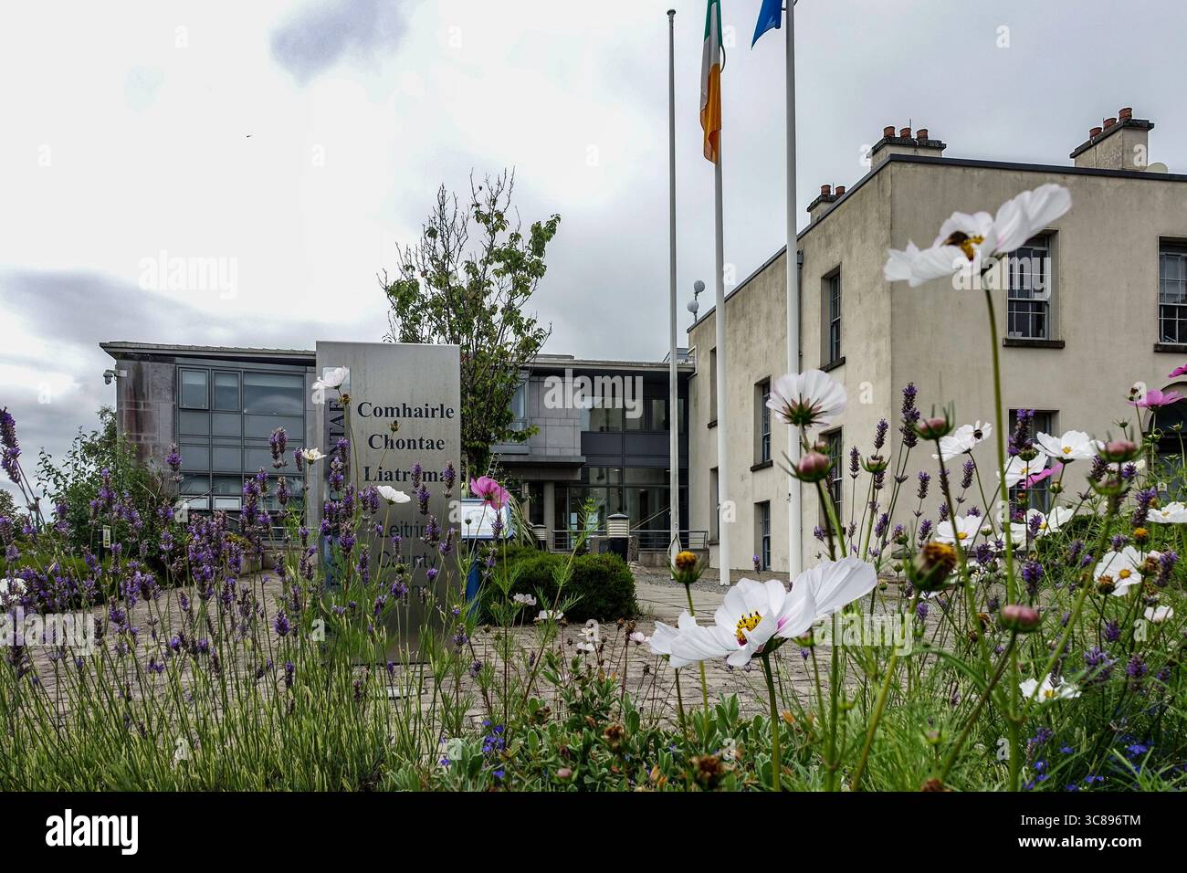 Uffici del Leitrim County Council (Comhairle Chontae Liatroma) a Carrick-on-Shannon, con fiori selvatici, bandiera irlandese e facciata moderna dell'edificio civico. Foto Stock