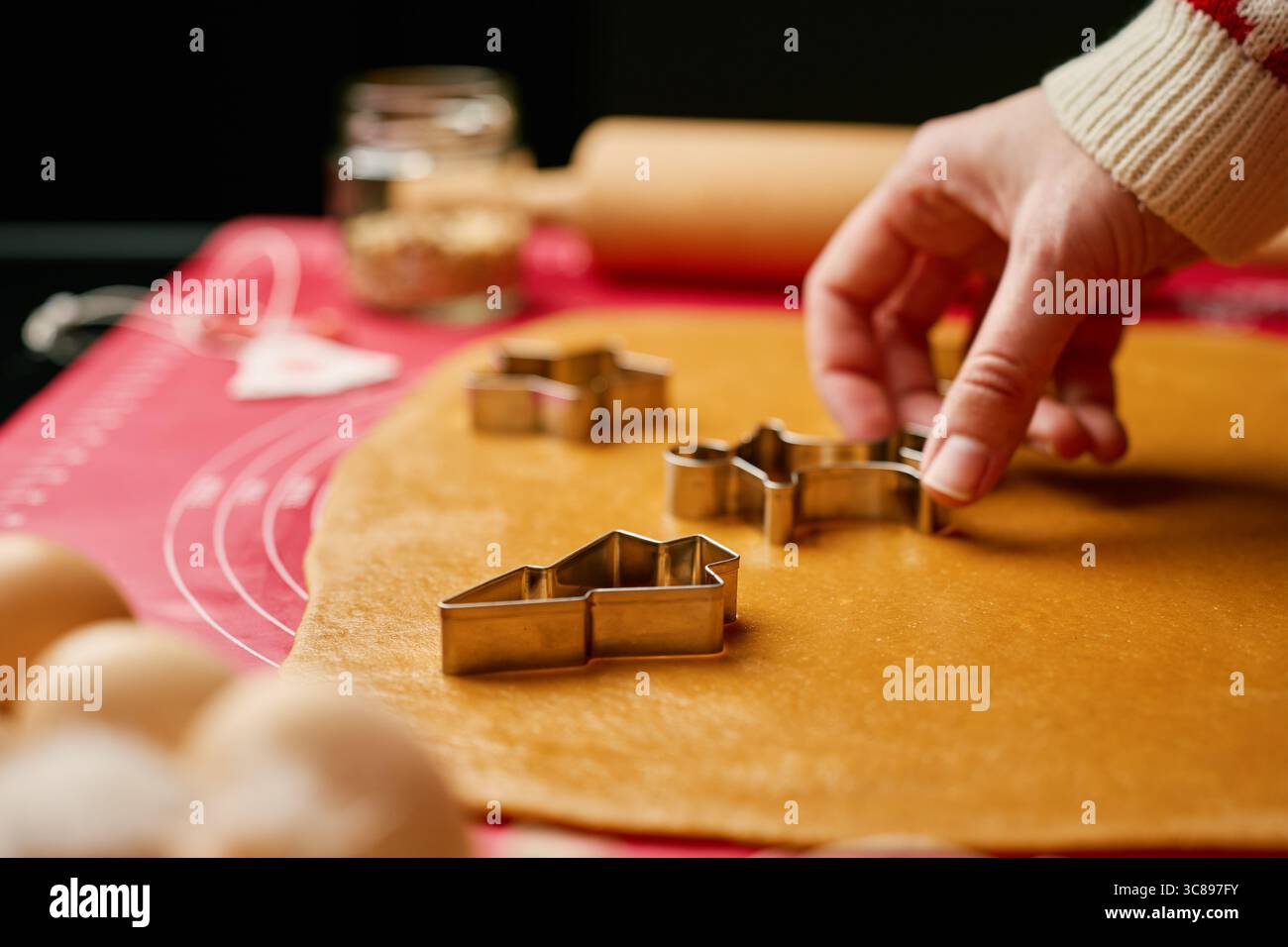 Primo piano delle mani premendo il tagliabasette in metallo nell'impasto di pan di zenzero sul tappetino da forno in silicone. Preparazione al forno per le feste e concetto di tradizione familiare Foto Stock