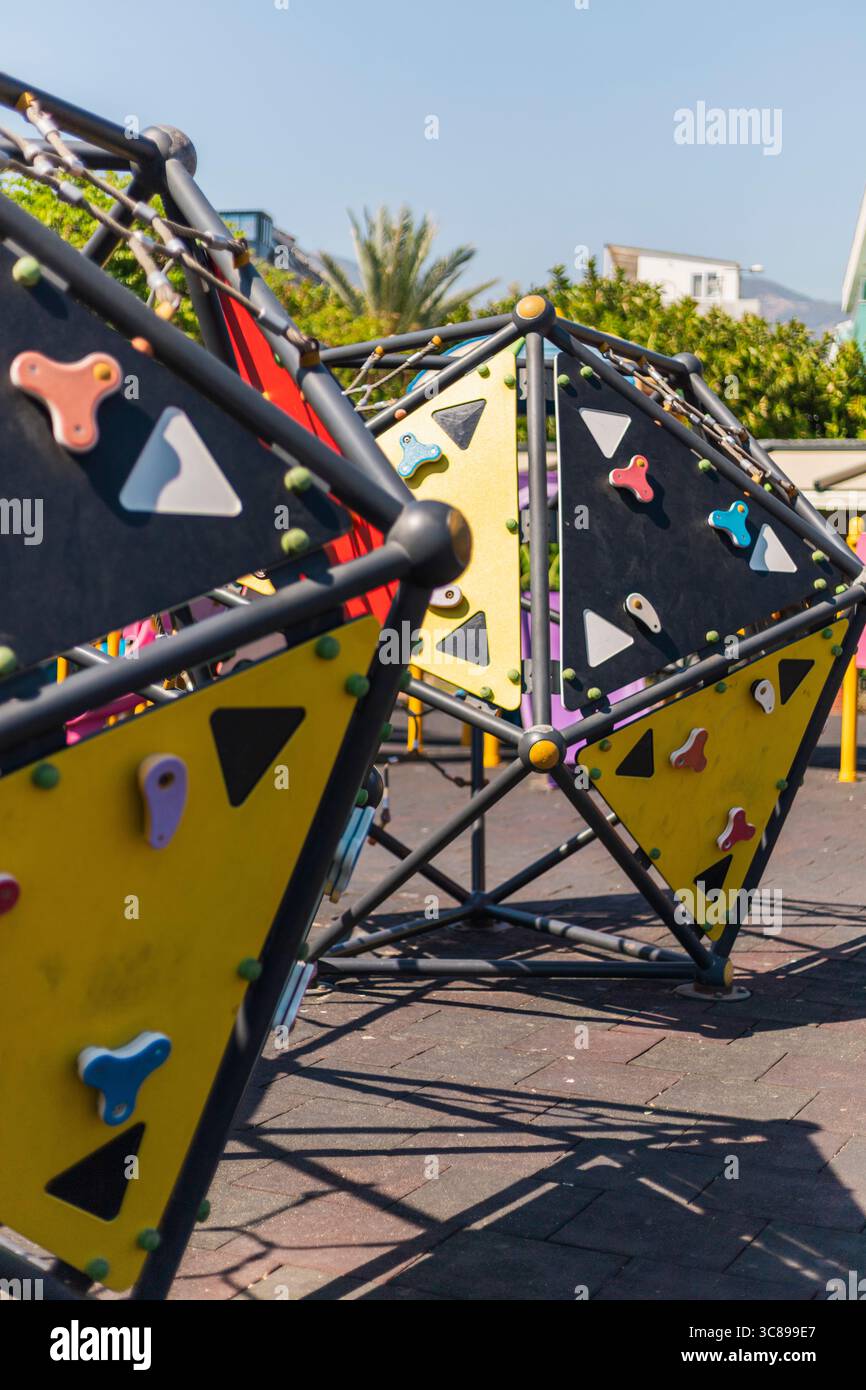 Le strutture di arrampicata dai colori vivaci invitano i bambini a giocare in modo attivo sotto un cielo azzurro. La vegetazione lussureggiante circonda il vivace parco giochi Foto Stock