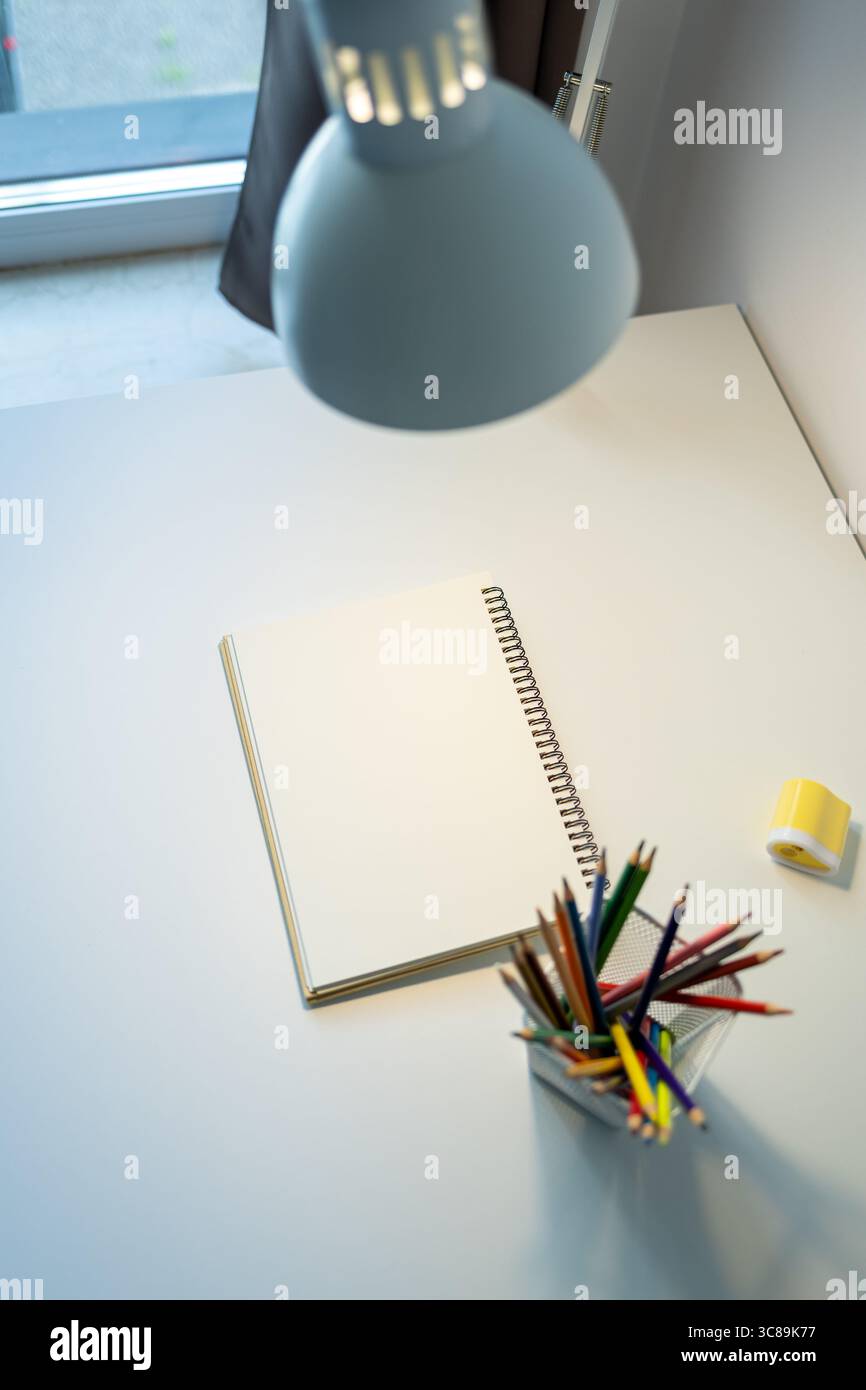 sketchbook illuminato da lampada e set di matite colorate su tavolo, disegno e hobby, concetto di ritorno a scuola Foto Stock
