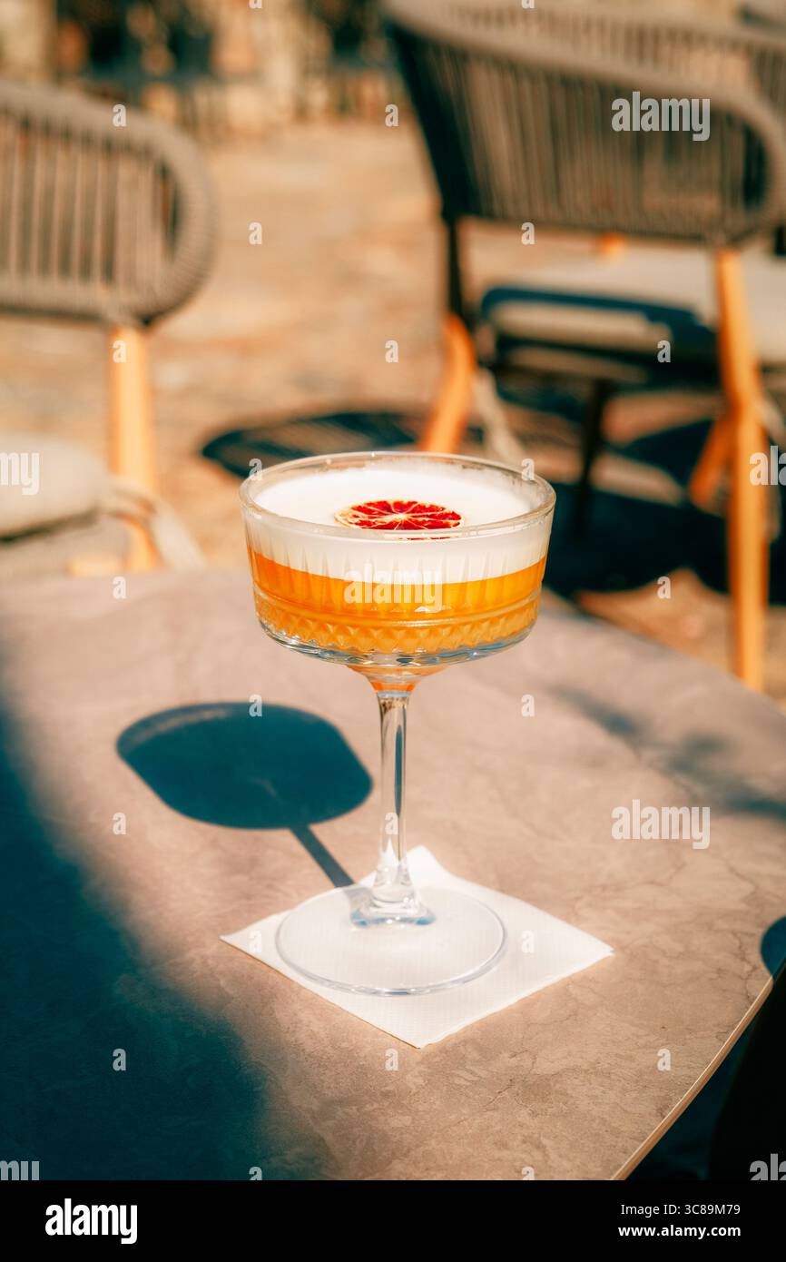 Elegante cocktail con schiuma e guarnizione di agrumi secchi servito su un soleggiato tavolo da caffè all'aperto Foto Stock