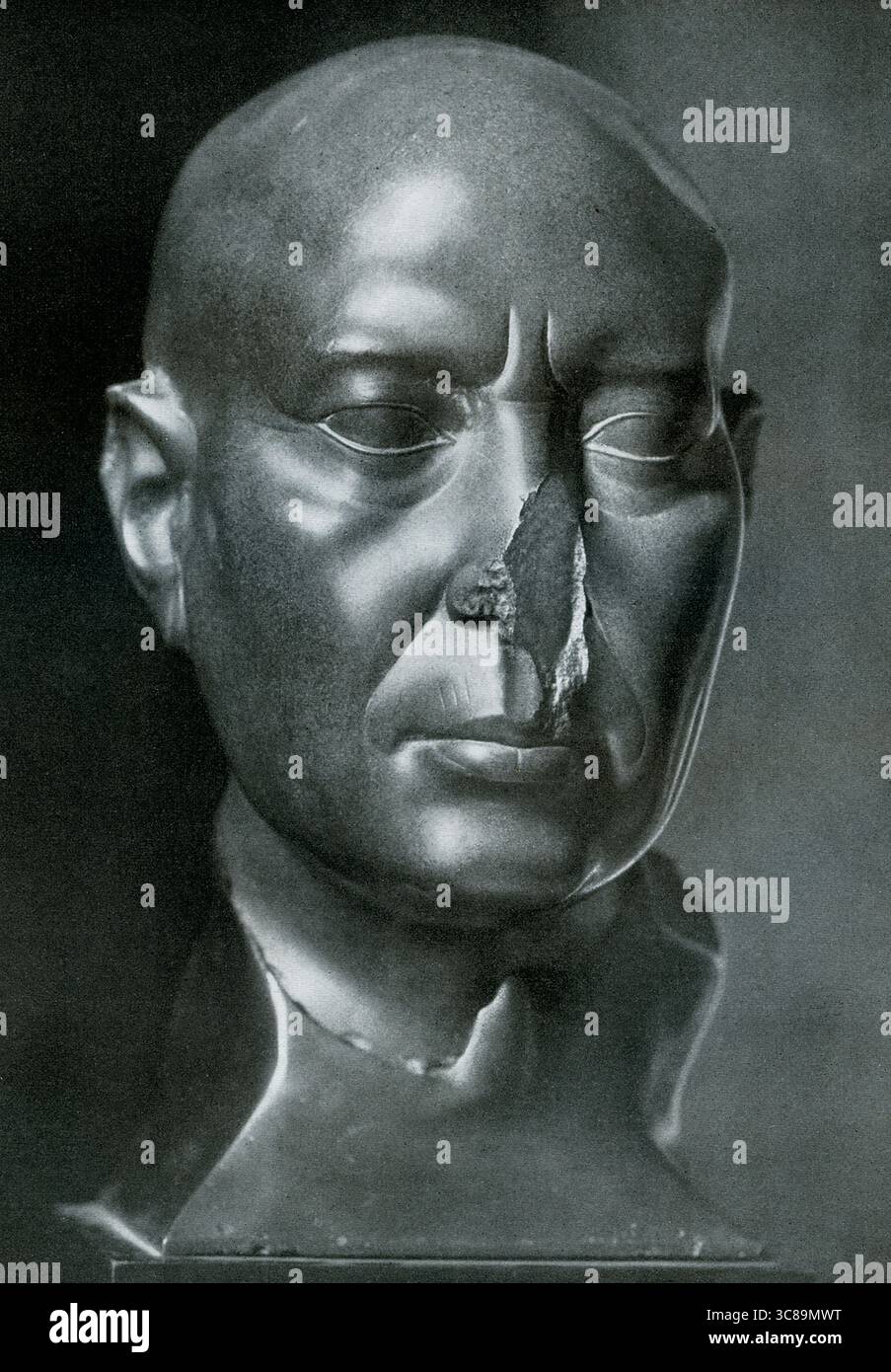 La didascalia del 1925 recita: "The Berlin Green Head from Memphis in Berlin State Museum. La "testa verde", scolpita all'inizio del IV secolo a.C. da una pietra verde-grigia nota come graywacke, fu scoperta nel 1857 e successivamente donata al Museum of fine Arts di Boston nel 1904. Intorno al 360 a.C., un ecclesiastico egiziano di alto rango commissionò una statua di se stesso da collocare in uno dei templi di Menfi, vicino all'attuale Cairo. Tuttavia, nel 343 a.C., il tempio fu saccheggiato dagli invasori, la statua spezzata in pezzi e l'edificio lasciato nel caos. Dopo aver cacciato gli invasori, gli egiziani colle Foto Stock