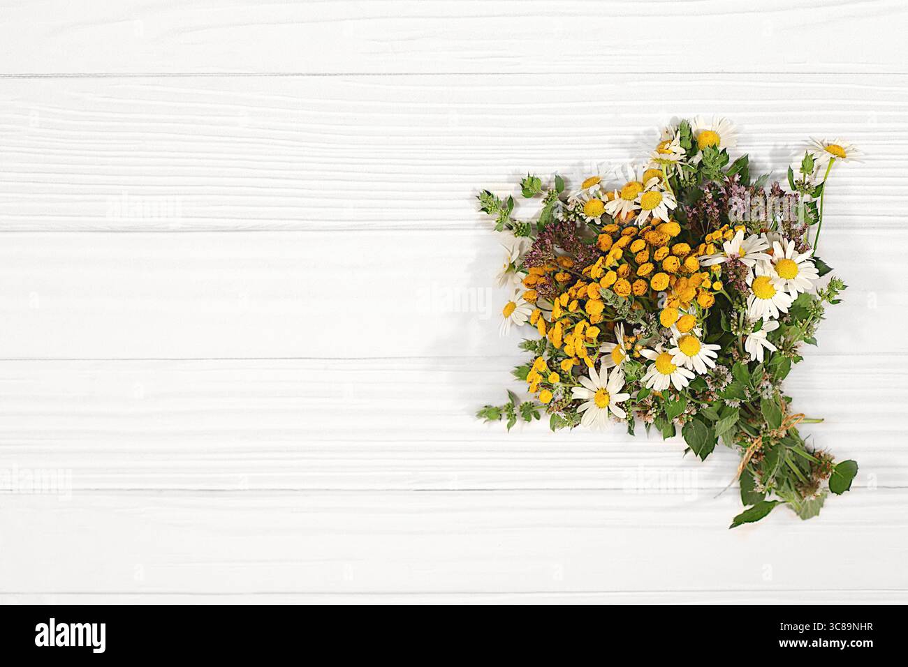 Composizione floreale di erbe e fiori selvatici su un tavolo di legno, stile rustico, bouquet di tansy, menta, celandina, camomilla e yarrow, raccolta di u Foto Stock